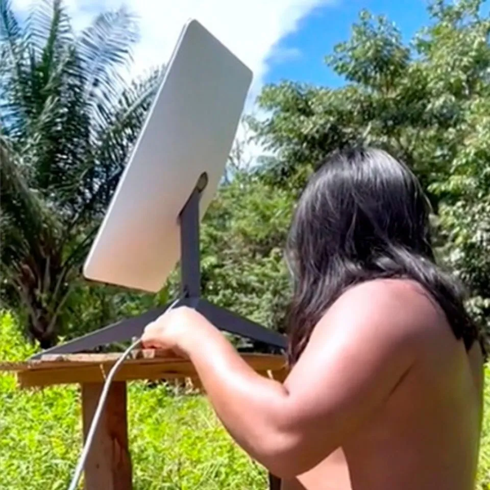 Influenciador digital Ind&iacute;gena Da Aldeia operando sua Starlink em meio a floresta.
